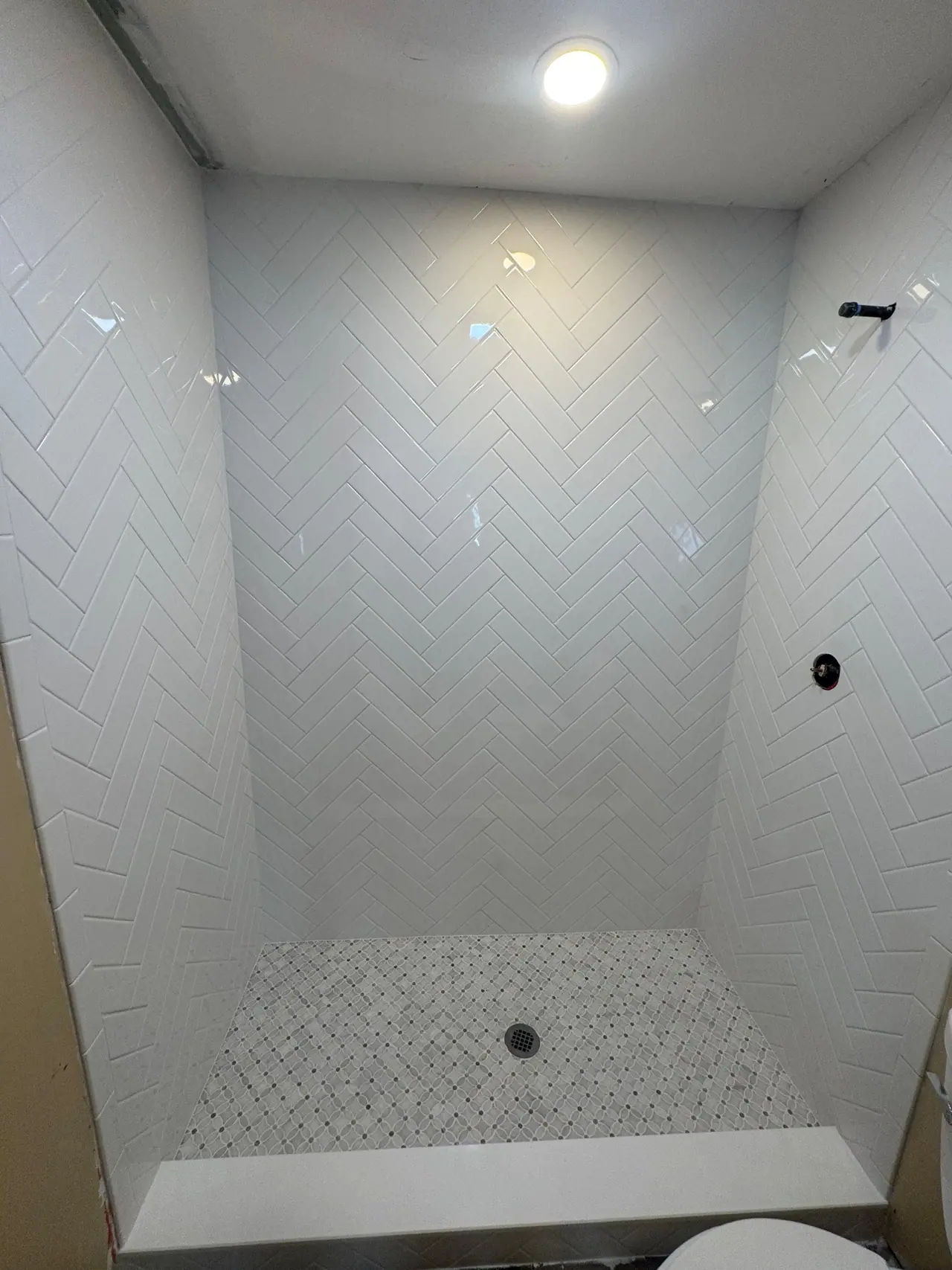 Full shower build — waterproof membrane, white herringbone subway walls, and a marble-look mosaic floor. — 3