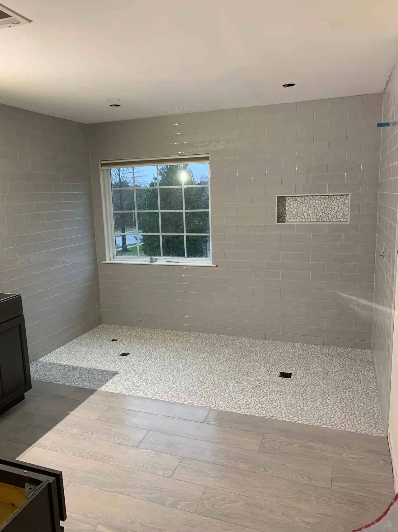 Walk-in shower with subway wall tile, pebble mosaic floor, and recessed niche detail. — 2